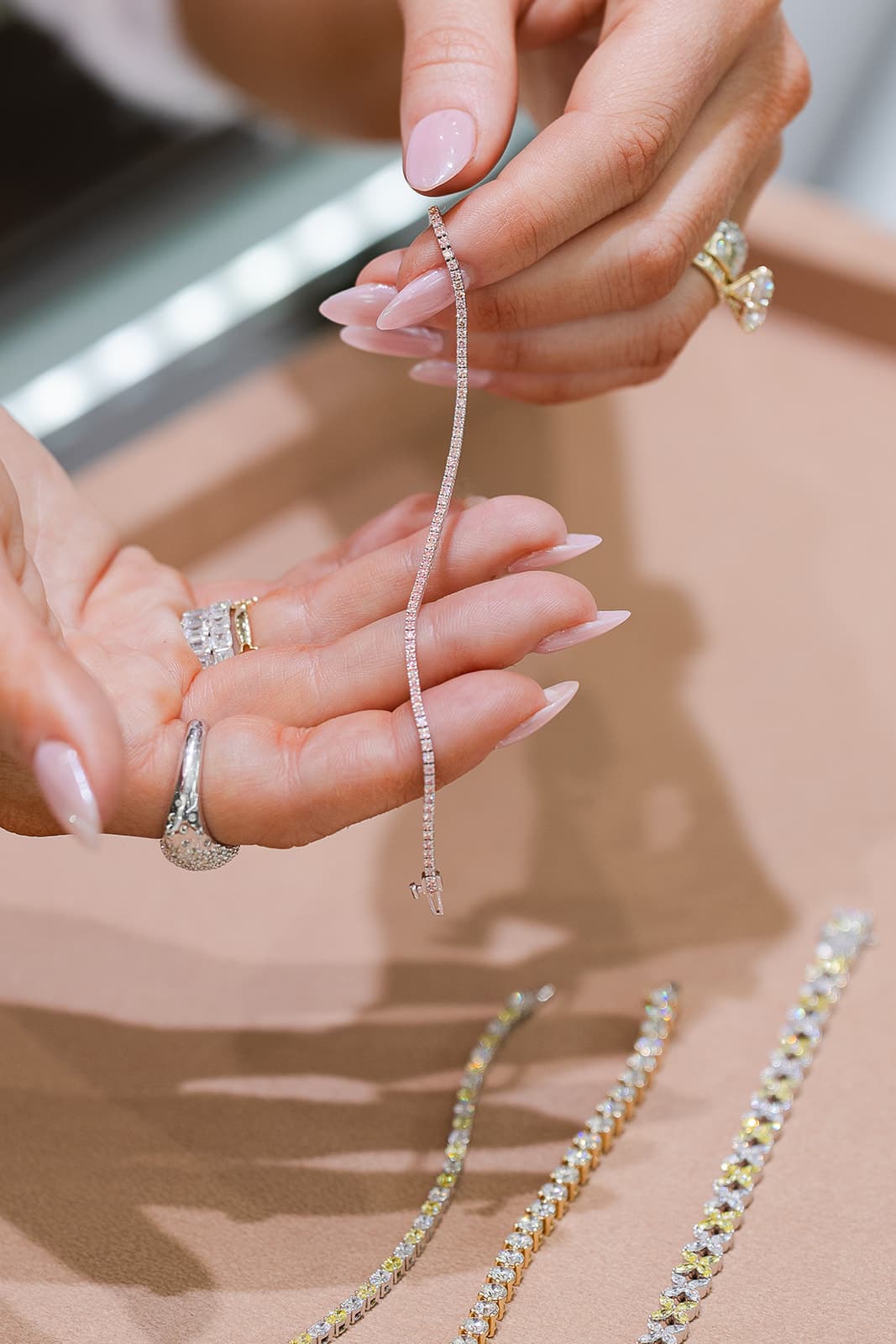 Hands holding a diamond tennis bracelet over a jewelry tray