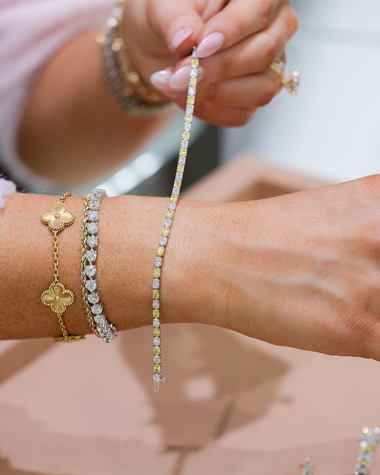 Stacked diamond and gold bracelets being styled on a wrist over peach suede