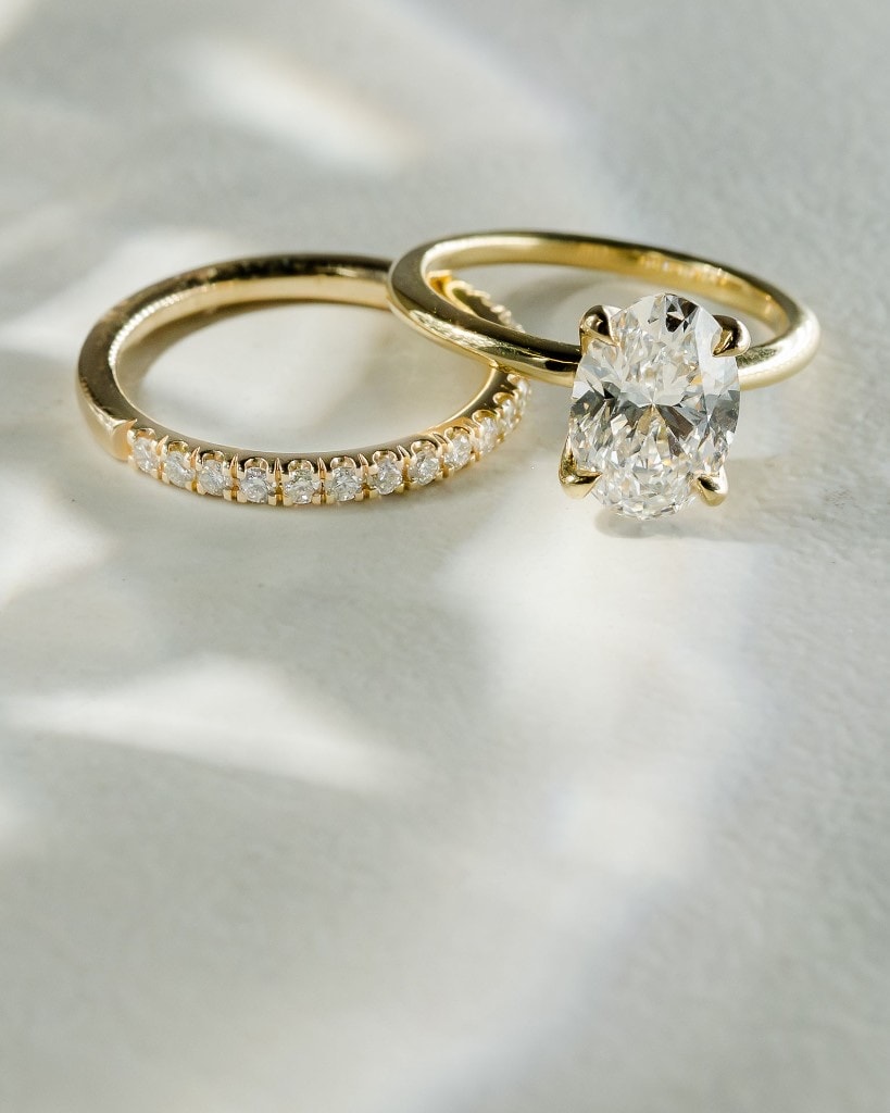 Oval solitaire engagement ring in yellow gold beside a matching diamond pavé wedding band