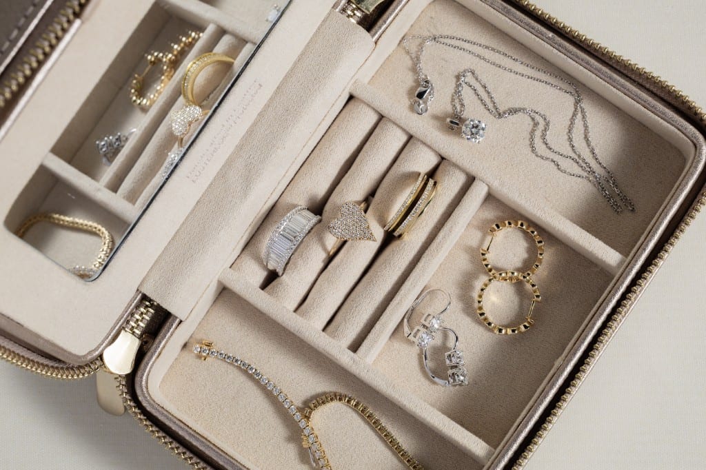 Open cream velvet travel jewelry case holding diamond rings, gold hoops, a tennis bracelet and a diamond pendant necklace