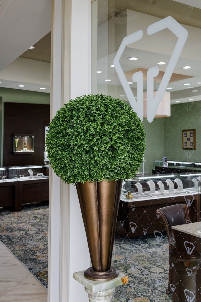 The entryway to the Giganti & Giganti showroom: a topiary in a brass urn beside the etched-glass diamond logo, with the cases visible beyond