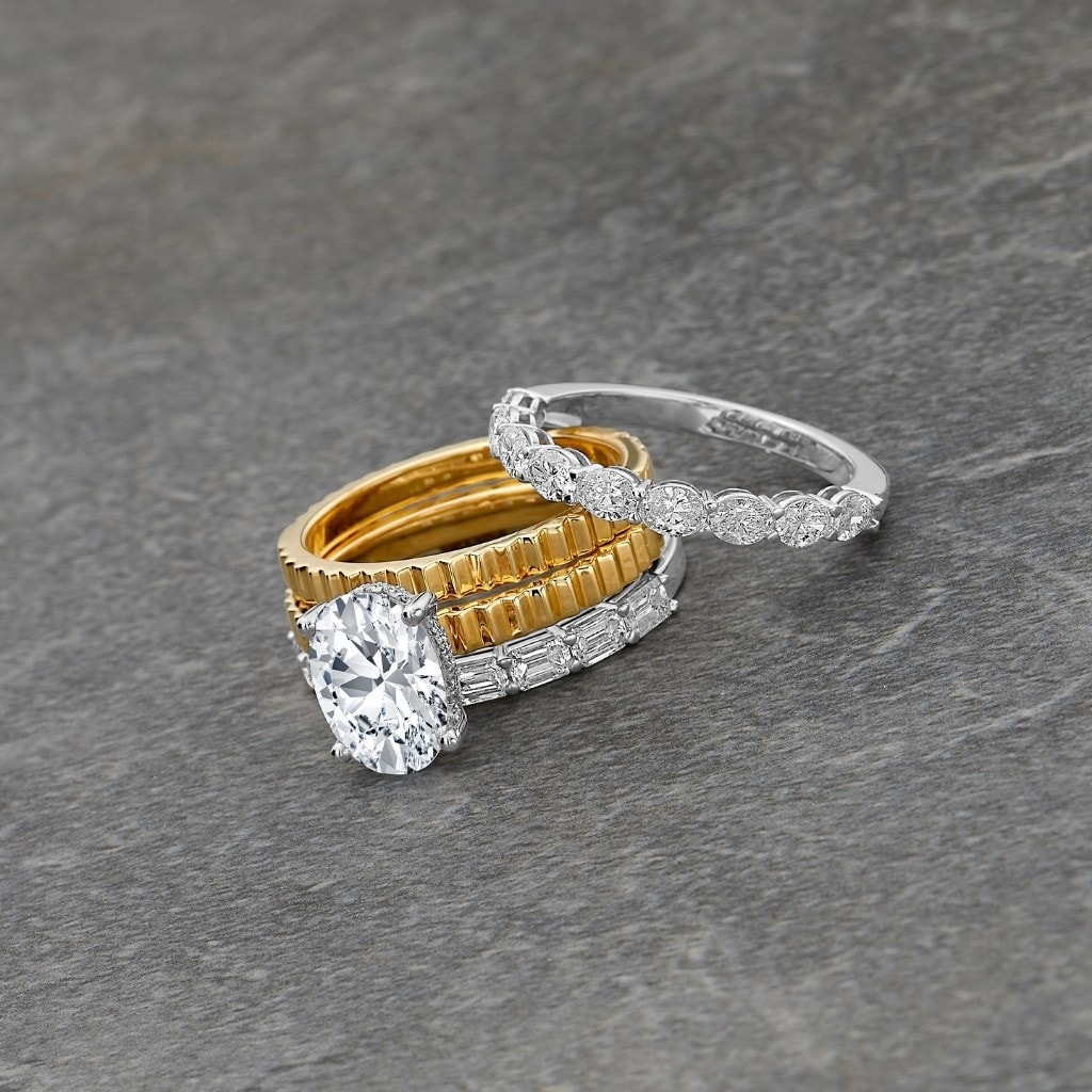 Oval diamond engagement ring stacked with fluted yellow gold and diamond eternity wedding bands on gray slate